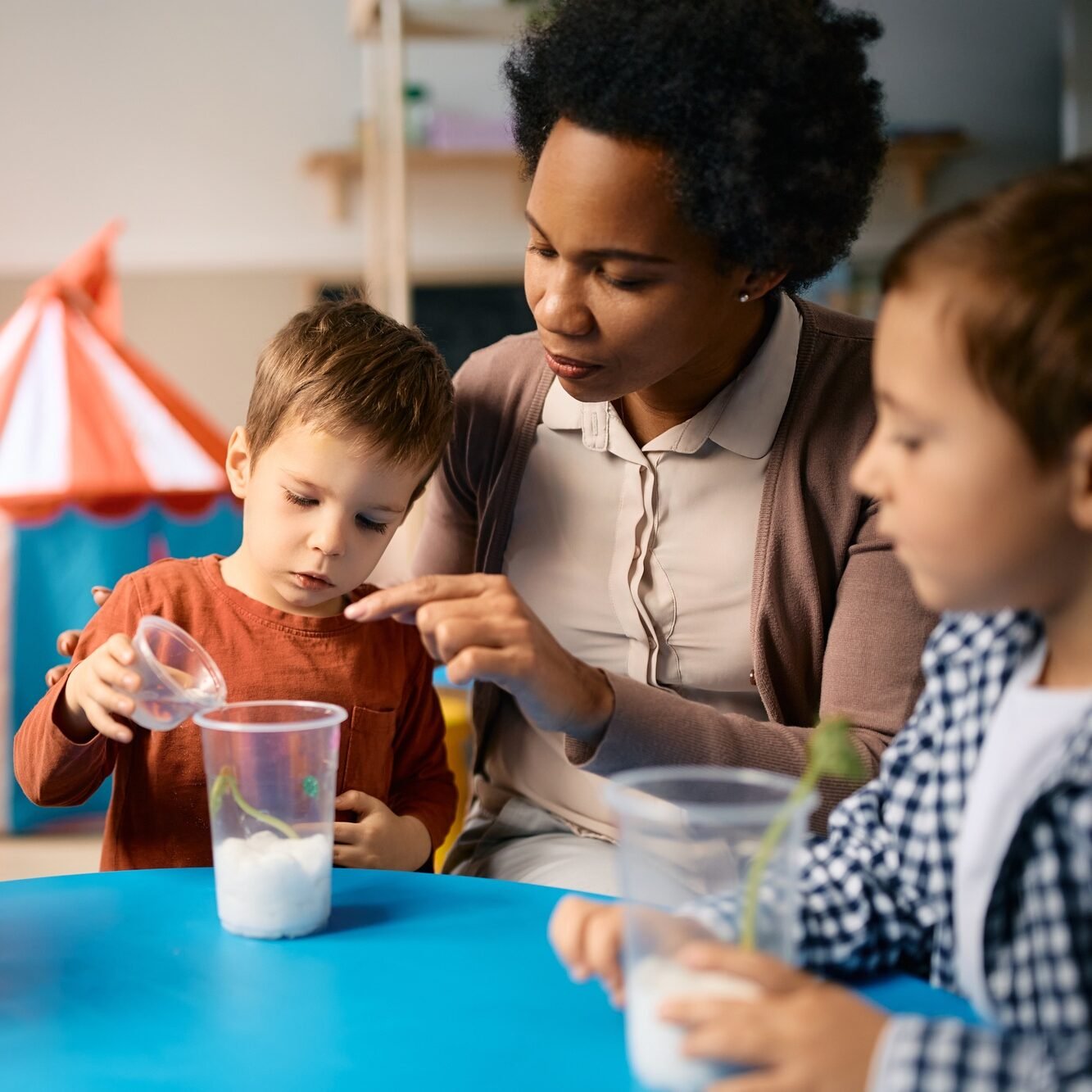 Black female teacher teaching group of kids to plant seeds at preschool.